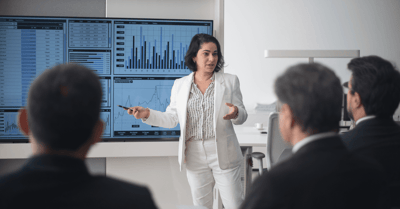 woman presenting in front of screen with graphs (1)-png